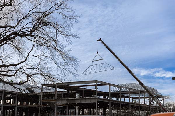 A crane lifts a roof support into place on top the clinical health sciences and wellness building under construction