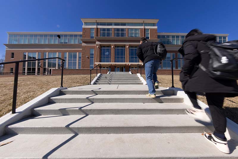Two students walk up the steps towards McVey Data Science under a clear blue sky