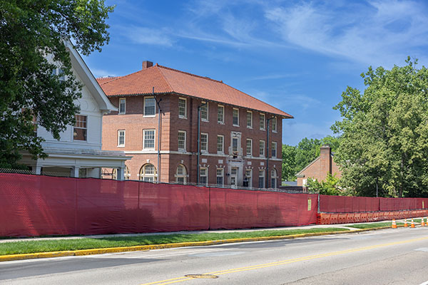 The exterior of Wells Hall surrounded by a red construction fence and Spring Street in the foreground
