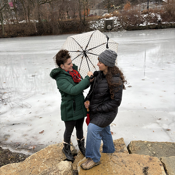 Journalist Rebecca Nagle interviews Kara Strass of the Myaamia Center on the bank of the St. Mary's River in Fort Wayne, Indiana. The river is frozen over and it was a windy day, so they're using an umbrella to block the wind.