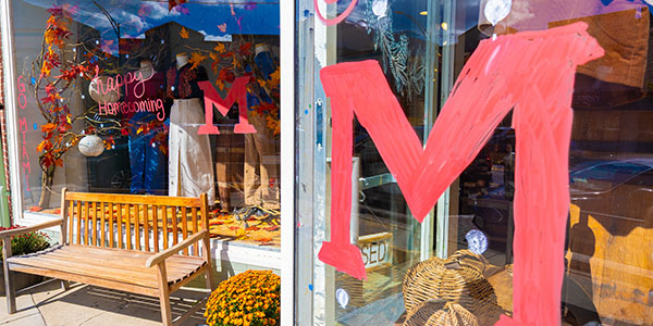 Two red block Ms on a storefront window and the words Happy Homecoming