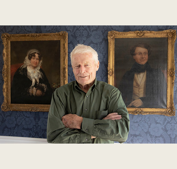 Richard Cocks poses between two oil paintings in his home